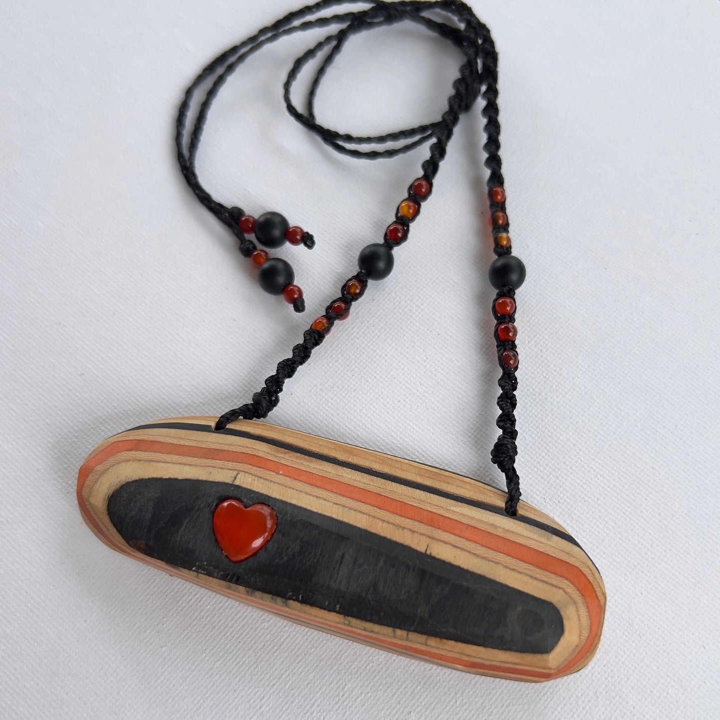 Handmade, unique recycled skateboard pendant with lush embedded Carnelian crystal heart on an adjustable macrame necklace cord woven with Obsidian and Carnelian.