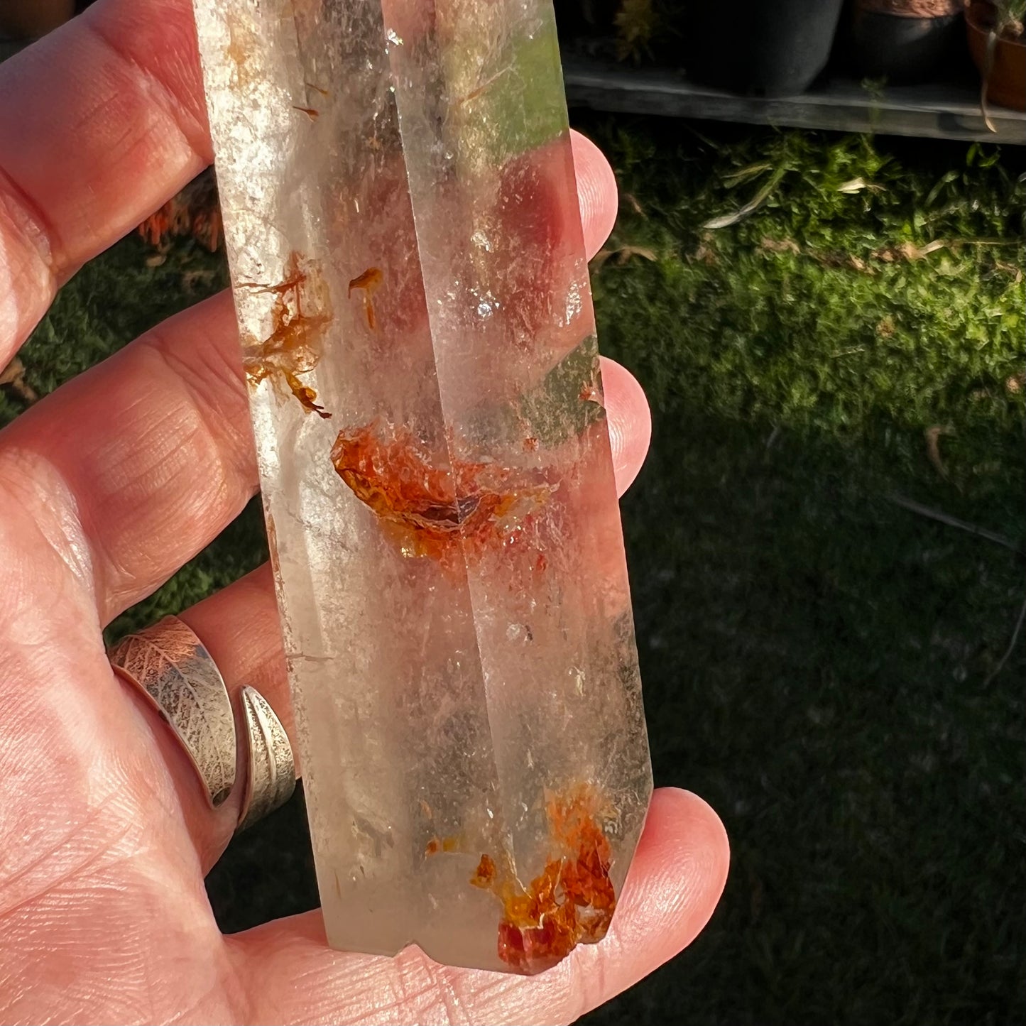 Clear crystal with red iron inclusions held in a hand against a natural background